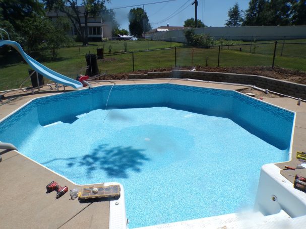 Octagonal swimming pool with a blue slide and clear water, surrounded by grass and trees.